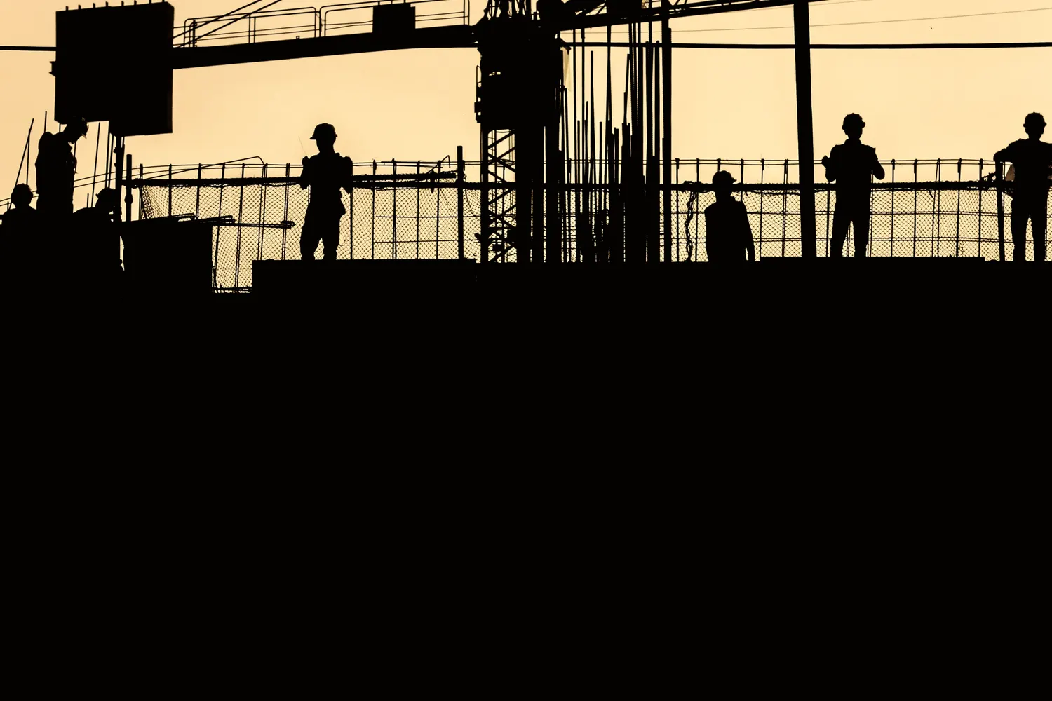 Silhouetted formwork and figures on an upper floor against a low evening sky.