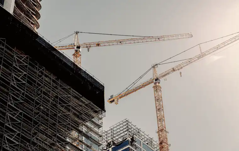 Two tower cranes crossing above scaffolding.